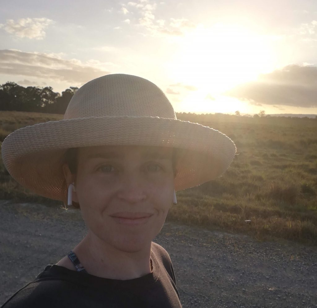 Selfie of Angela walking along a track through a field as the sun is setting.