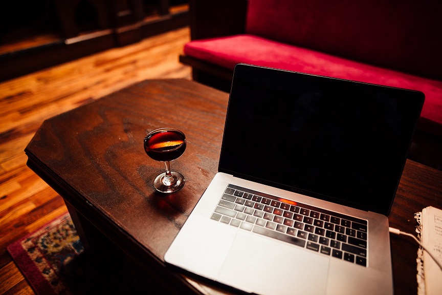 Glass of red wine sitting on a wooden coffee table, along with a laptop.